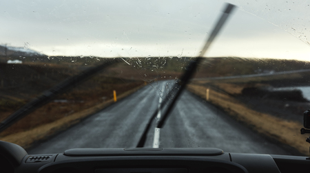 On the road in rainy day, car windshield with wipers cleaning rain dropsの写真素材