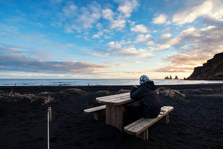 a man sitting on wooden bench at Black Sand Beach in sunsetの写真素材