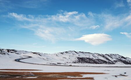 Landscaped in winter with country road and lenticular cloud on blue skyの写真素材