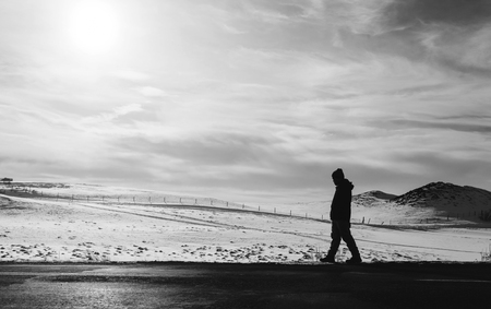 a man walking away on an empty desolated roadの写真素材