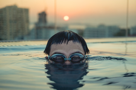 Close-up young man head shot in swimming pool in summer sunsetの写真素材