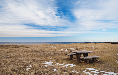 Wooden seat with table in empty field with blue skyの写真素材