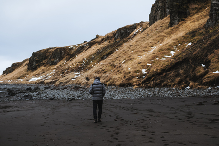 a man walking alone on black sand beach with cliffの写真素材