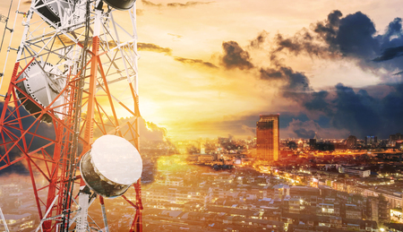 Double exposure telecommunication towers with TV antennas and satellite dish in sunset, with city backgroundの写真素材