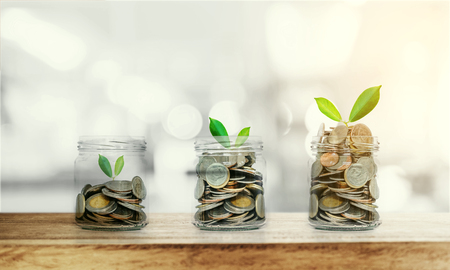 Money growing concepts, bottle of coins with growing plants on wooden table and Bokeh background, with sunlightの写真素材
