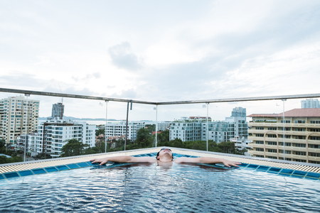 a man relaxing in swimming pool, with city view backgroundsの写真素材