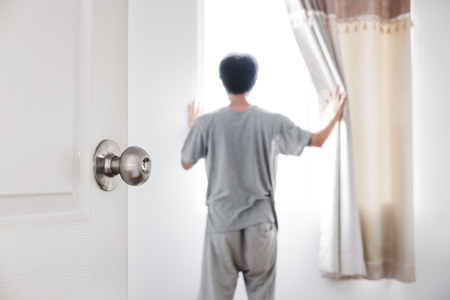 Door opened to the room, with a man open curtain receiving sunlight in the morningの写真素材