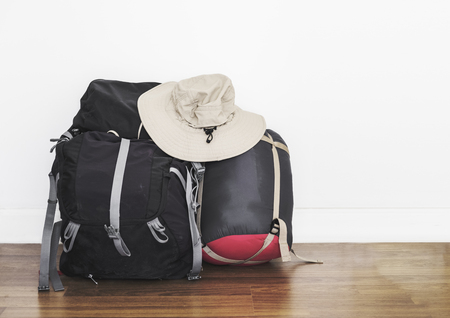 Backpack with sleeping bag and adventure hat, on wooden floor with white wall, baggage for traveling