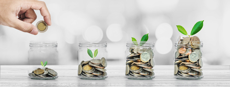 Saving money and investment concepts, Hand putting coin in glass bottles with plants glowingの写真素材