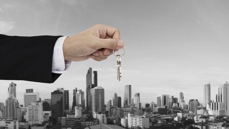 Hand holding keys with Bangkok city background, buying home, real estate and house rental conceptsの写真素材