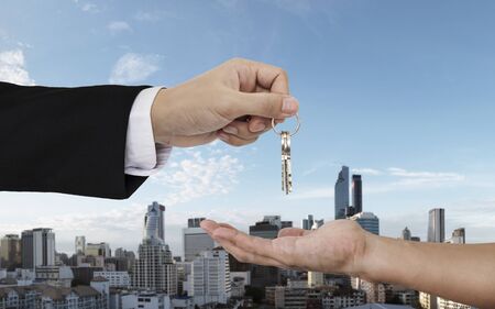 Hand giving and receiving keys with city background, buying home, real estate and house rental conceptsの写真素材