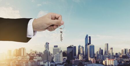 Hand holding keys with Bangkok city background, buying home, real estate and house rental conceptsの写真素材