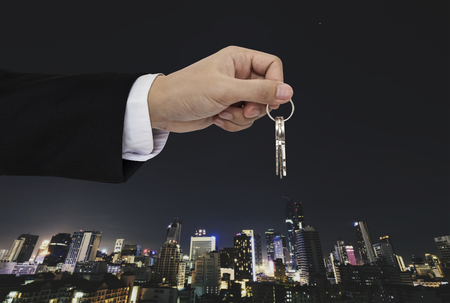 Hand holding keys with city background, real estate and property conceptsの写真素材