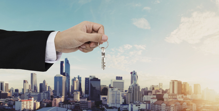 Hand holding keys with city backgroundの写真素材