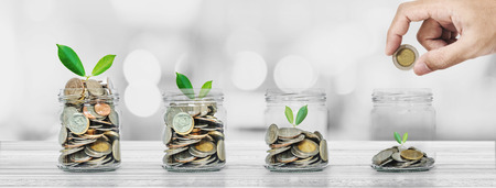 Saving money, Banking and Investment concepts, Panoramic Hand putting coin in glass bottles with plants glowingの写真素材