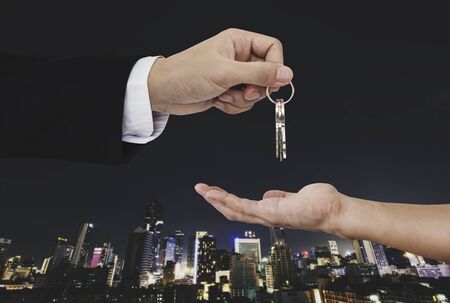 Hand holding keys with city background, real estate and property conceptsの写真素材
