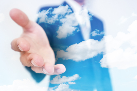 Businessman stretch out hand, with double exposure blue sky and white cloud backgroundの写真素材