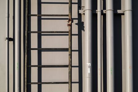 Electric and water pipelines and ladder, on industrial wall background