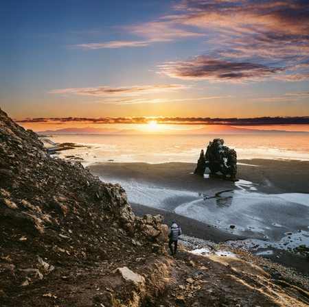 Landscape Hvitserkur in Iceland, young traveling hiking down from cliff to black sand beach in sunsetの写真素材