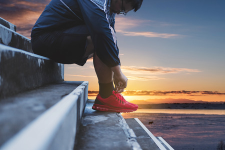 A Guy Tying Running Shoe, Preparing for Running in the Morning, with Sky in Sunrise backgroundの写真素材