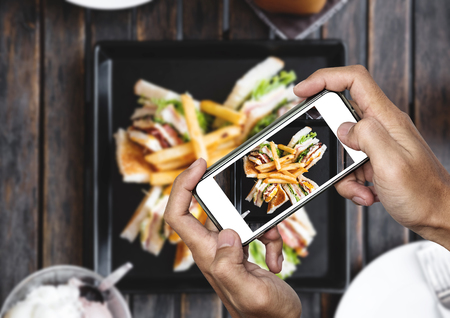 Taking food photo, food photography by smart phone, club sandwich with french fries on wooden tableの写真素材
