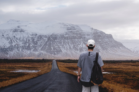 Young man with backpack walking alone on the country roadの写真素材