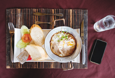 Breakfast fried eggs pan and bread, with water and smartphone, top viewの写真素材