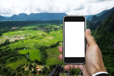 Hand holding smart phone, on the mountain beautiful nature view, empty white screen for copy spaceの写真素材