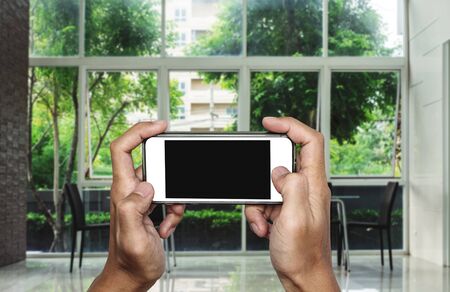 Hand using mobile phone, blank copy space on screen, interior living space backgroundの写真素材