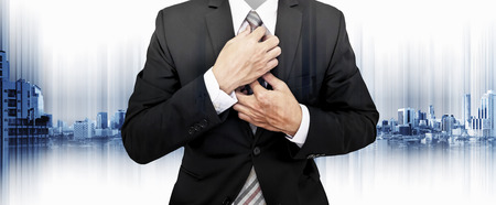 Businessman in black suit holding tie, with modern buildings in the city backgroundの写真素材