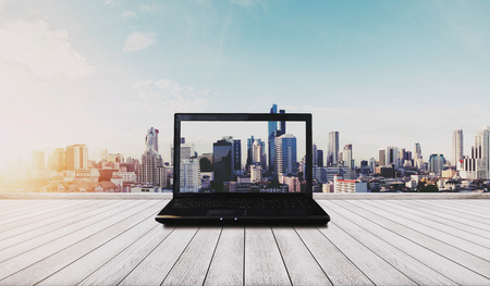Computer laptop on white wood floor with Bangkok city view in sunrise backgroundの写真素材