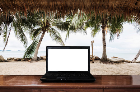 Computer laptop on wooden table, at the beach in summer. Clipping path empty white screenの写真素材