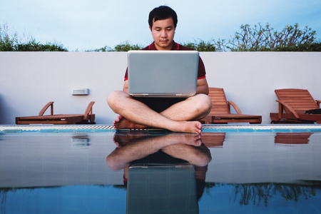 a man working on laptop computer, sitting at poolsideの写真素材