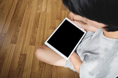 a man using digital tablet computer on wooden floor, in casual clothing, blank empty device screenの写真素材