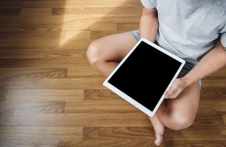 a man using digital tablet computer on wooden floor, in casual clothing, blank empty device screen, above viewの写真素材