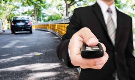 Businessman holding car remote controller with modern car driving on the road backgroundの写真素材