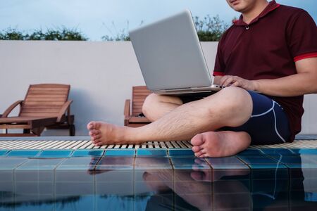 a man working on laptop computer, sitting at poolside, selective focusの写真素材