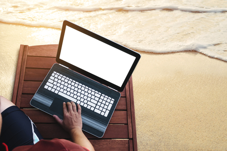 a man using computer laptop on wooden sunbath lounge chair on the beach in summer at sunset. Clipping path computer notebook screenの写真素材