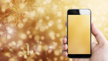 Hand holding mobile smart phone, luxury gold Bokeh light with fireworks backgroundの写真素材