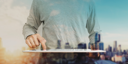 Asian guy using digital tablet with double exposure defocus city in sunrise backgroundの写真素材