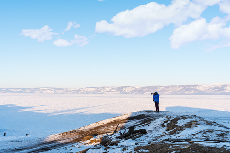 Traveller photographer taking photograph on cliff at lake Baikal, Russia in winterの写真素材