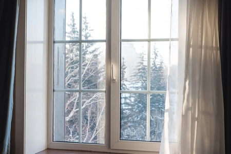 White window frame with curtain blowing by wind, winter scenic view in the morningの写真素材