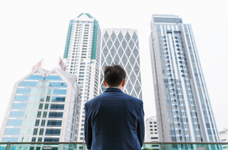 Young businessman standing on balcony looking at modern buildings in Bangkok city, Thailandのeditorial素材