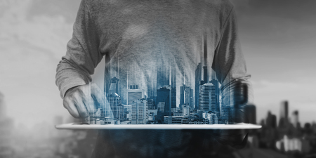 a man using digital tablet, and modern buildings hologram. Real estate business and building technology conceptの写真素材