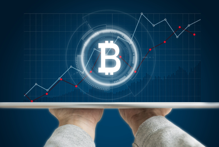 Hand holding digital tablet with B symbol of Bitcoin, internet banking and block chain and raising graph backgroundの写真素材