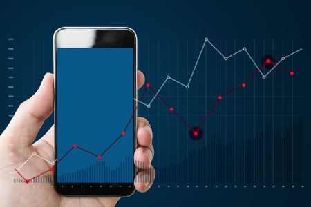 Hand holding mobile smart phone, and raising graph on blue backgroundの写真素材