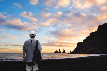 a man with backpack standing on black sand beach in sunset, Iceland. Vacation travelling in summer...