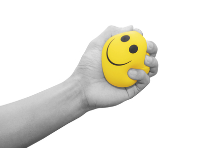 Hand squeezing smiling face yellow stress ball, isolated on white backgroundの写真素材