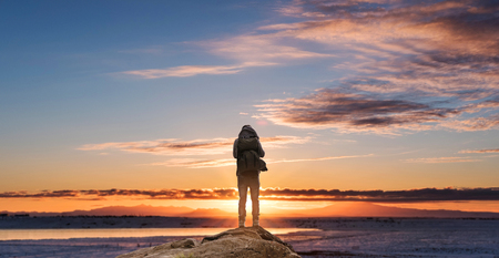 a man with backpack standing on the rock enjoying sunrise in the morningの写真素材