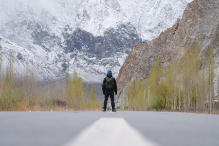 a man with backpack standing on empty road in northern Pakistanの写真素材